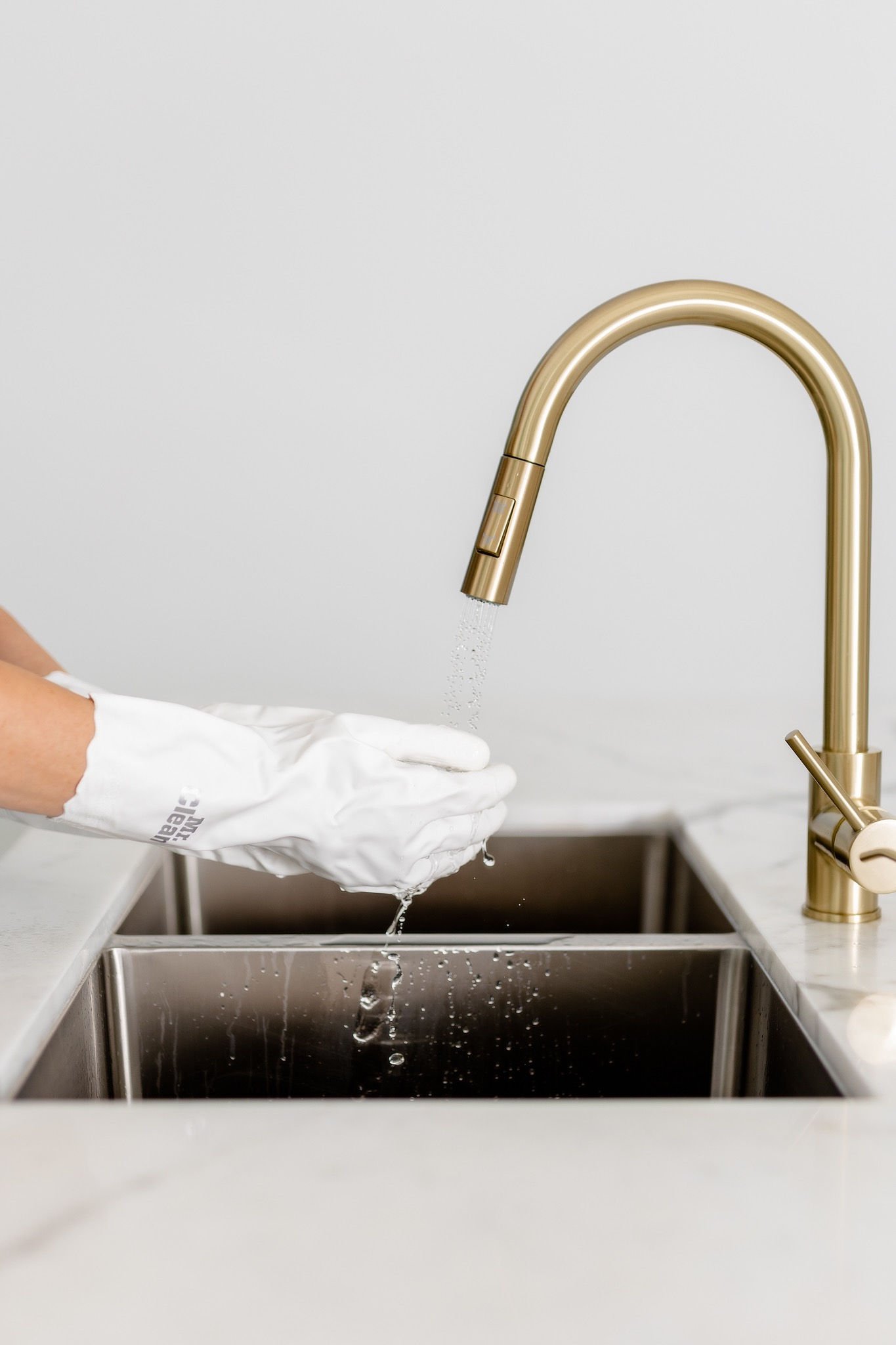 A gloved hand cleaning a gold faucet over a stainless steel sink